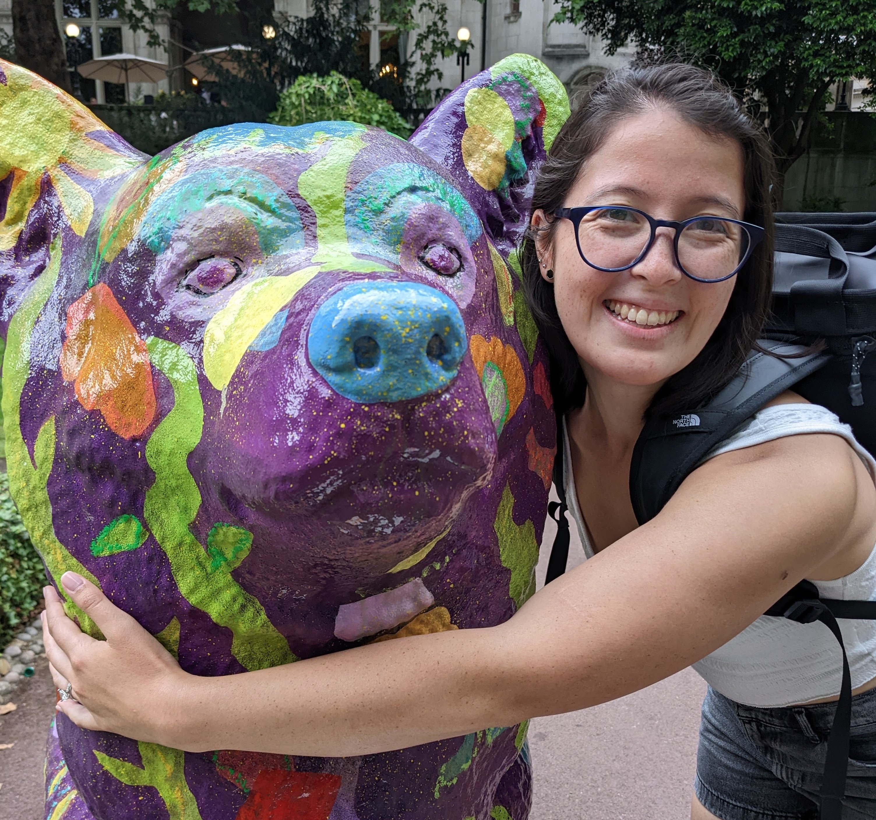 half-asian female with short dark brown hair and glasses hugging a large corgi statue painted purple with flowers
